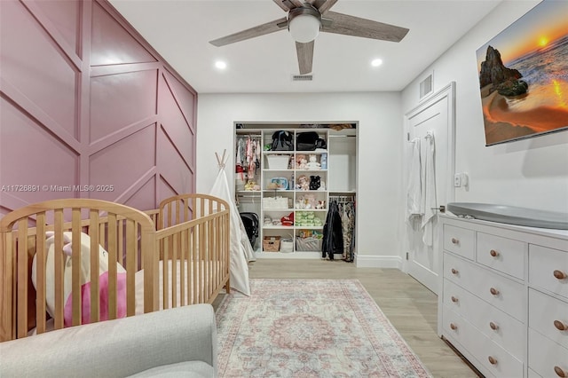 bedroom with ceiling fan, a closet, light hardwood / wood-style flooring, and a nursery area