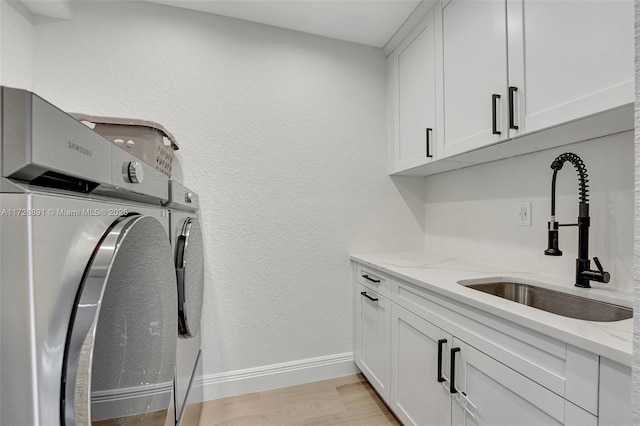 clothes washing area with light hardwood / wood-style flooring, washing machine and dryer, sink, and cabinets