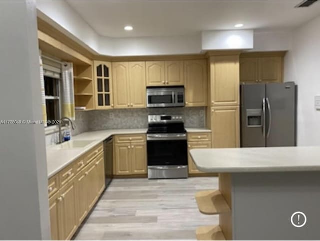 kitchen with stainless steel appliances, light hardwood / wood-style floors, sink, backsplash, and light brown cabinetry