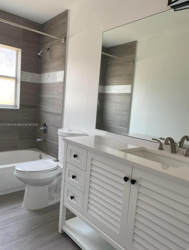 full bathroom featuring toilet, tiled shower / bath combo, hardwood / wood-style floors, and vanity