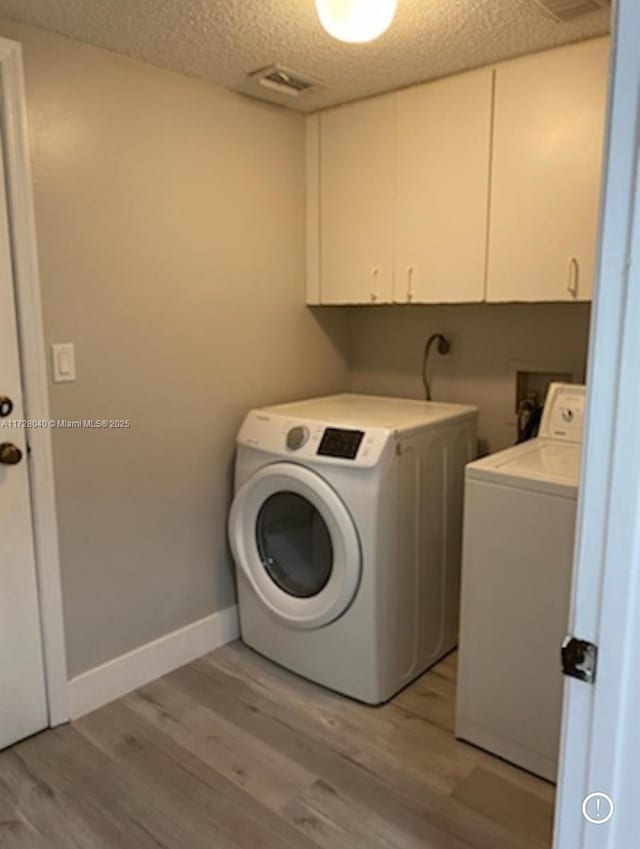 laundry room with washing machine and dryer, cabinets, a textured ceiling, and light wood-type flooring