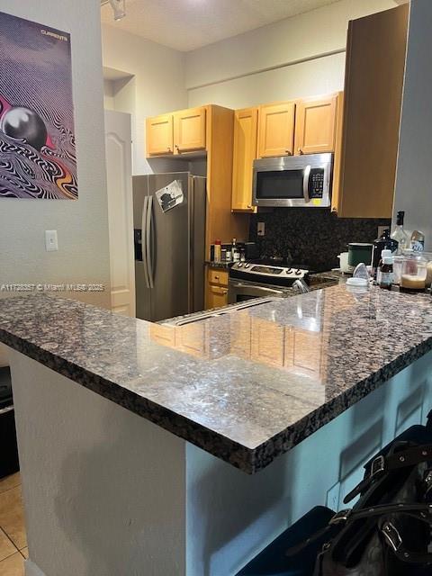 kitchen featuring a kitchen bar, appliances with stainless steel finishes, kitchen peninsula, and light tile patterned flooring