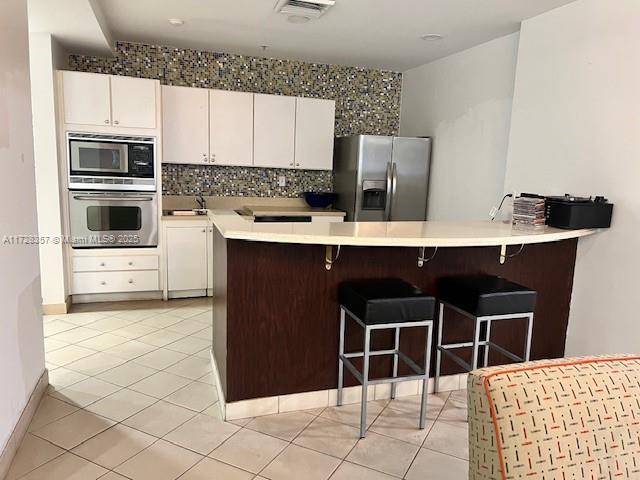 kitchen with a kitchen bar, white cabinetry, appliances with stainless steel finishes, and light tile patterned flooring