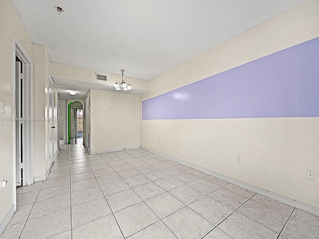 unfurnished room with a textured ceiling, a chandelier, and light tile patterned flooring