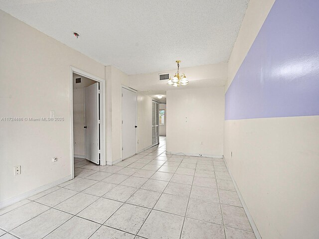 tiled empty room with a textured ceiling and a chandelier