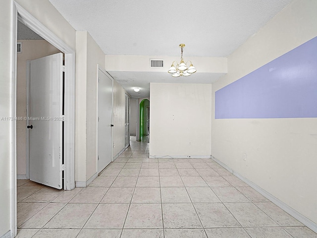 empty room featuring a textured ceiling, light tile patterned floors, and a notable chandelier