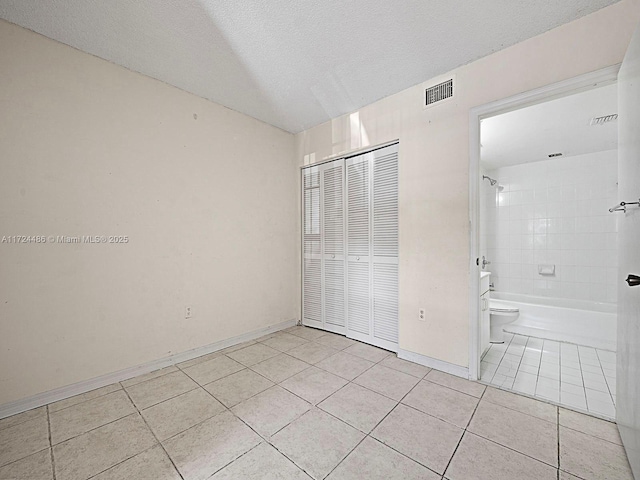 unfurnished bedroom with a textured ceiling, light tile patterned floors, a closet, and ensuite bathroom