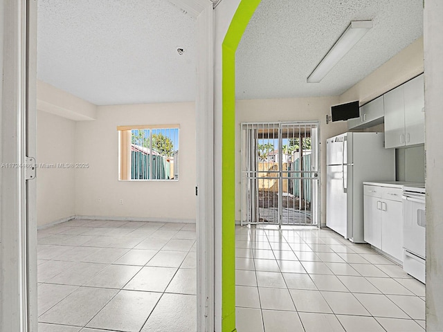 kitchen featuring white cabinets, light tile patterned floors, white appliances, and a textured ceiling