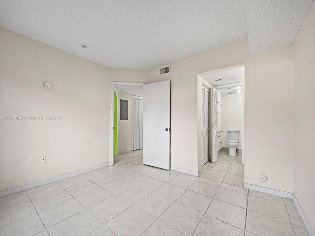 unfurnished bedroom featuring a textured ceiling, light tile patterned floors, ensuite bath, and electric panel