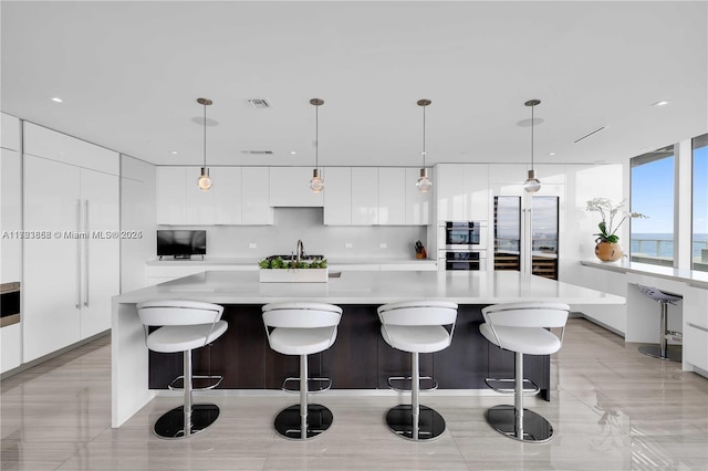 kitchen featuring a spacious island, white cabinetry, a kitchen bar, and hanging light fixtures