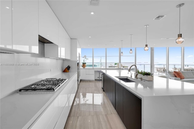 kitchen with sink, a water view, white cabinets, a center island with sink, and decorative light fixtures