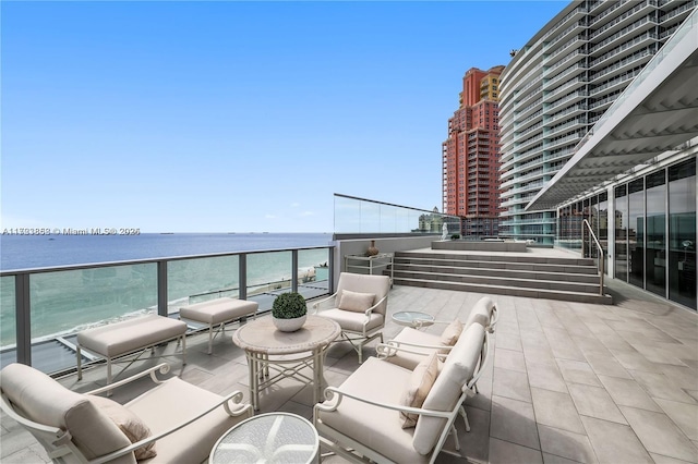 view of patio / terrace with a water view, a balcony, and a view of the beach