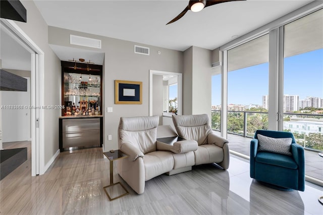 living room featuring ceiling fan, a wall of windows, and bar area