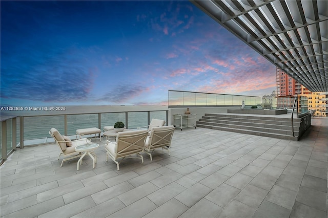 patio terrace at dusk with a balcony, a water view, and outdoor lounge area