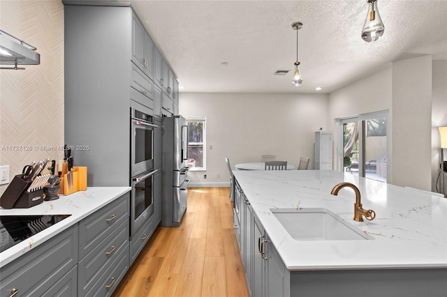 kitchen featuring light stone countertops, black electric stovetop, sink, hanging light fixtures, and gray cabinets