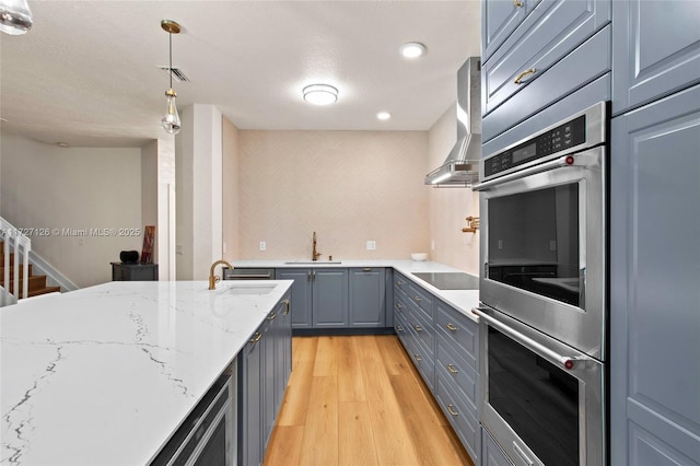 kitchen with pendant lighting, exhaust hood, double oven, sink, and light stone counters