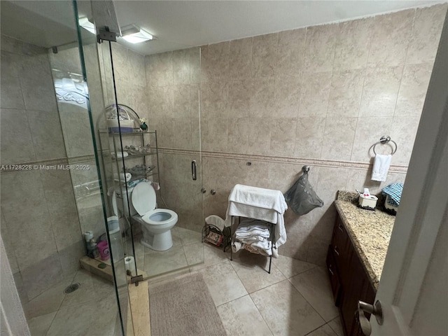 bathroom featuring toilet, vanity, tile patterned flooring, tile walls, and a shower with shower door