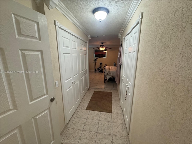 hallway with light tile patterned floors, ornamental molding, and a textured ceiling