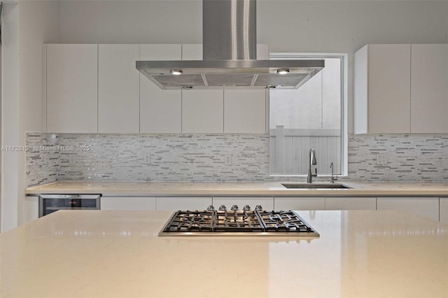 kitchen with stainless steel gas stovetop, white cabinetry, island range hood, decorative backsplash, and sink