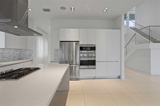 kitchen with white cabinets, appliances with stainless steel finishes, island exhaust hood, backsplash, and light tile patterned floors