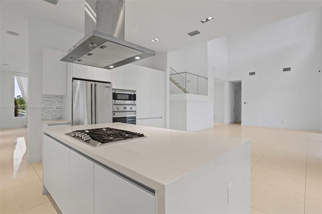 kitchen with white cabinets, appliances with stainless steel finishes, a kitchen island, island exhaust hood, and light tile patterned floors