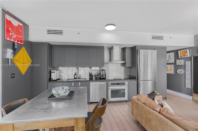 kitchen featuring backsplash, wall chimney range hood, sink, light hardwood / wood-style flooring, and appliances with stainless steel finishes