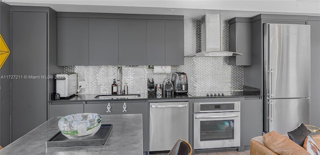 kitchen featuring gray cabinetry, backsplash, appliances with stainless steel finishes, and wall chimney exhaust hood