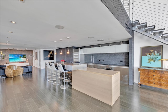 kitchen with a kitchen island, white cabinetry, sink, hanging light fixtures, and a breakfast bar