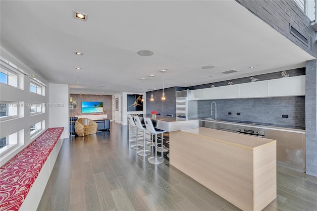 kitchen with pendant lighting, white cabinets, decorative backsplash, a kitchen breakfast bar, and a large island