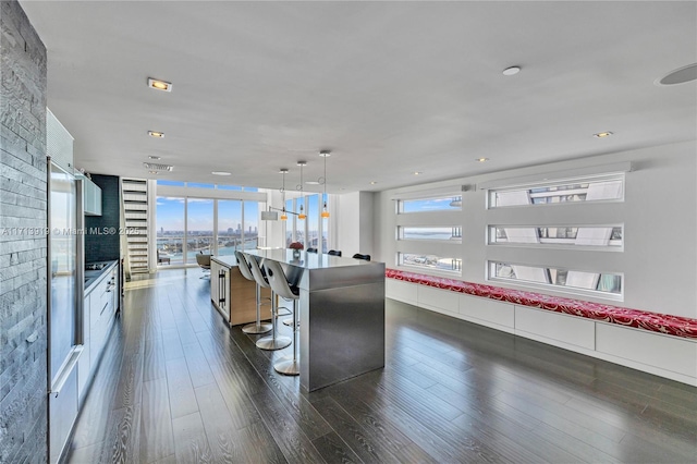 kitchen with a kitchen bar, a spacious island, dark wood-type flooring, pendant lighting, and white cabinets