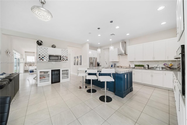 kitchen featuring a kitchen bar, an island with sink, appliances with stainless steel finishes, decorative light fixtures, and wall chimney range hood