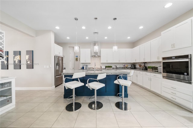 kitchen featuring light stone countertops, appliances with stainless steel finishes, a center island with sink, and wall chimney range hood