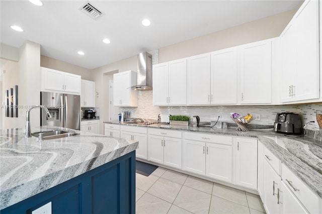 kitchen featuring white cabinets, stainless steel refrigerator with ice dispenser, wall chimney range hood, and decorative backsplash