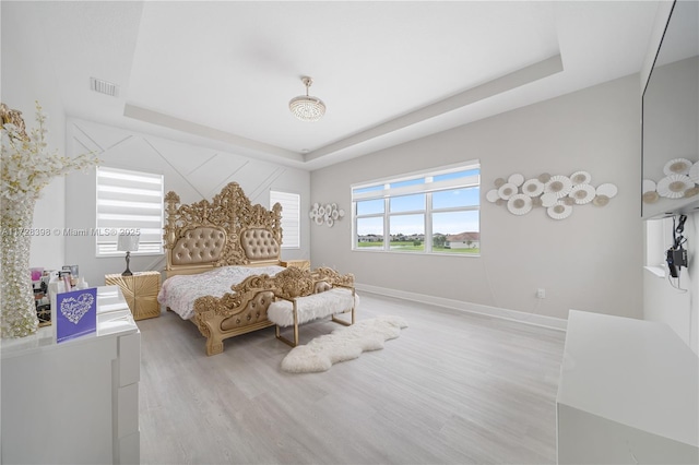 bedroom with light wood-type flooring and a tray ceiling