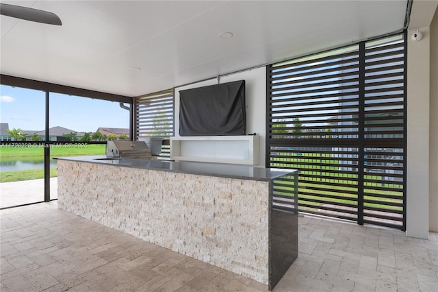 view of patio with a water view, an outdoor kitchen, ceiling fan, and area for grilling