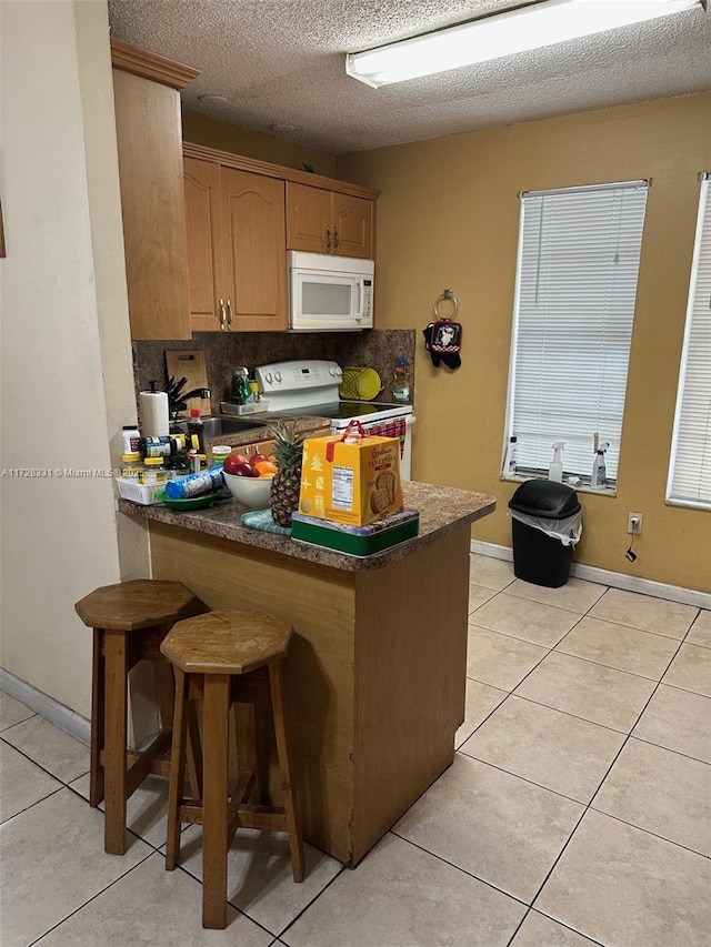 kitchen with a textured ceiling, light tile patterned floors, kitchen peninsula, and white appliances