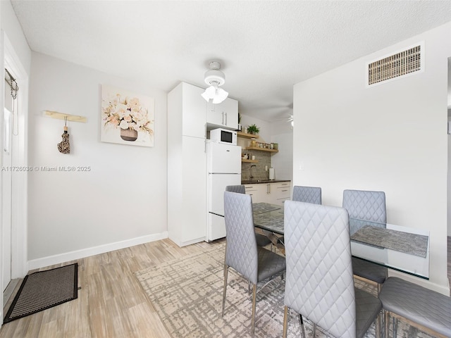 dining room with light wood-type flooring, ceiling fan, a textured ceiling, and sink