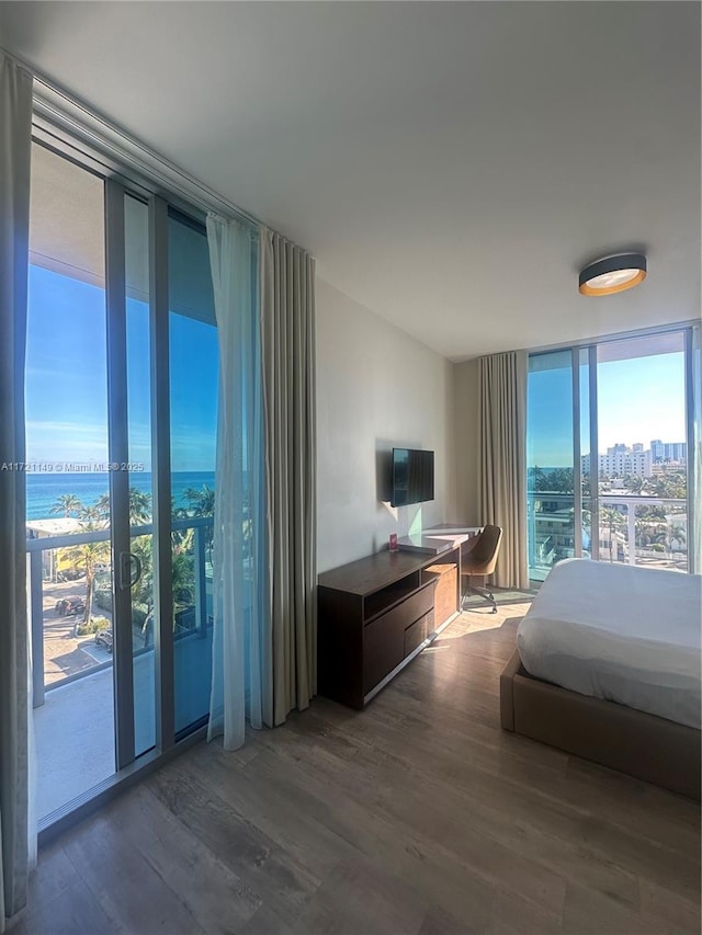 bedroom featuring hardwood / wood-style flooring, access to exterior, a wall of windows, and a water view