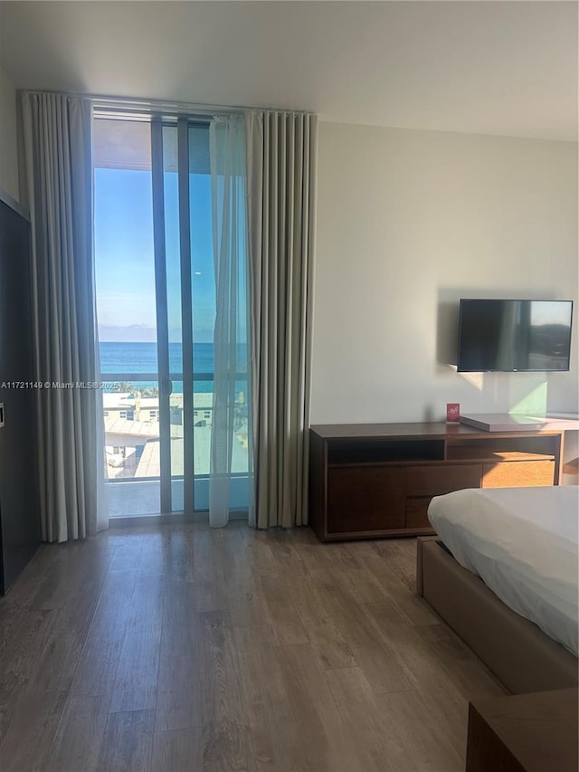 bedroom with a wall of windows, a water view, and dark hardwood / wood-style floors