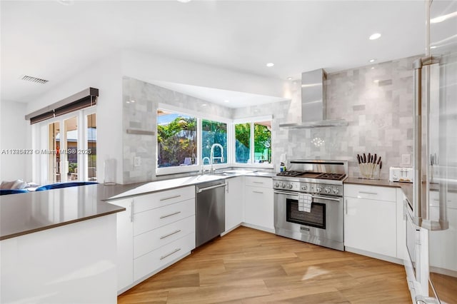 kitchen featuring wall chimney exhaust hood, plenty of natural light, stainless steel appliances, and white cabinetry