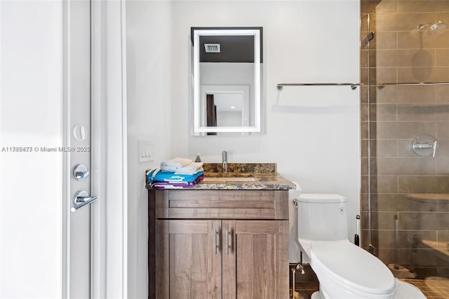 bathroom with toilet, vanity, and a tile shower