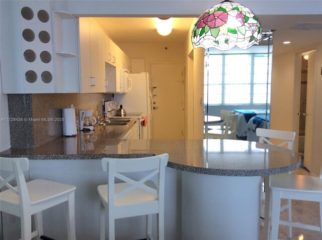 kitchen featuring white cabinets, kitchen peninsula, backsplash, and a breakfast bar