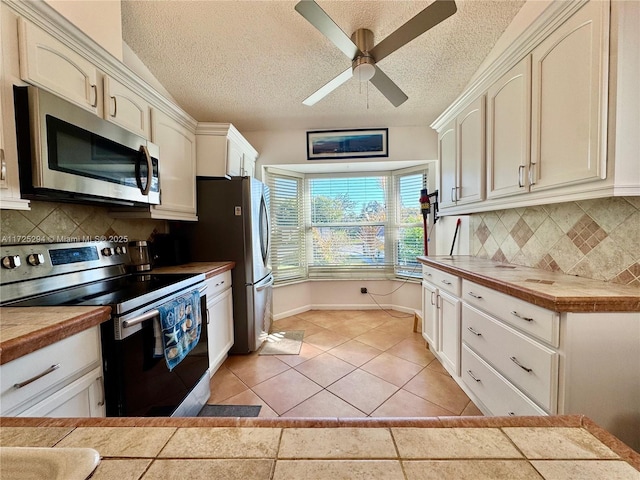 kitchen featuring light tile patterned floors, tile countertops, ceiling fan, appliances with stainless steel finishes, and backsplash