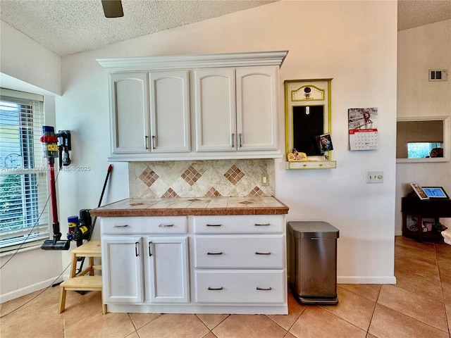 kitchen with light tile patterned floors, white cabinetry, lofted ceiling, and tasteful backsplash