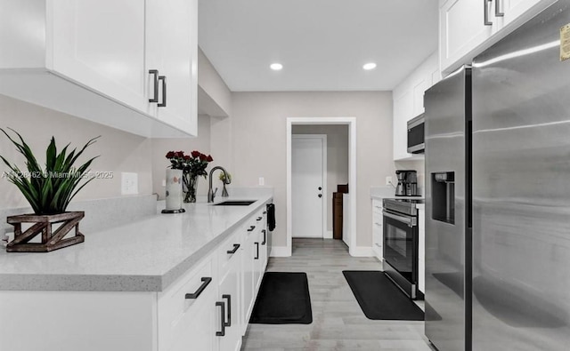 kitchen featuring white cabinetry, stainless steel appliances, sink, light stone counters, and light hardwood / wood-style flooring