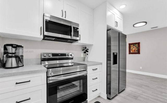 kitchen with appliances with stainless steel finishes, light hardwood / wood-style floors, white cabinets, and light stone countertops