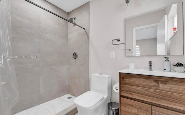 bathroom with toilet, a tile shower, and vanity