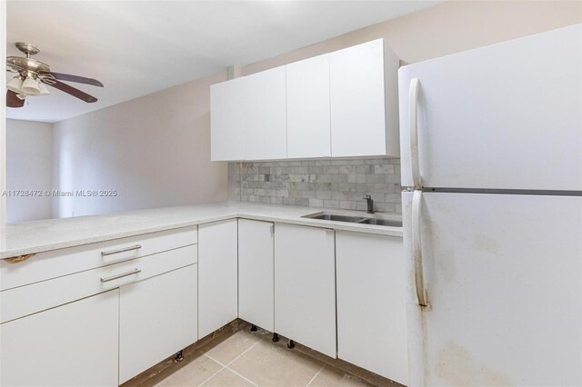 kitchen featuring white fridge, light tile patterned floors, backsplash, white cabinets, and sink