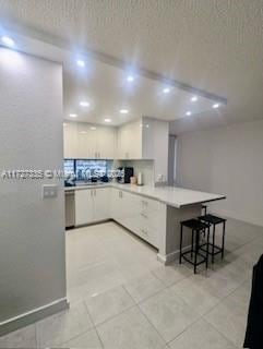 kitchen featuring a breakfast bar, kitchen peninsula, decorative backsplash, light tile patterned flooring, and white cabinetry