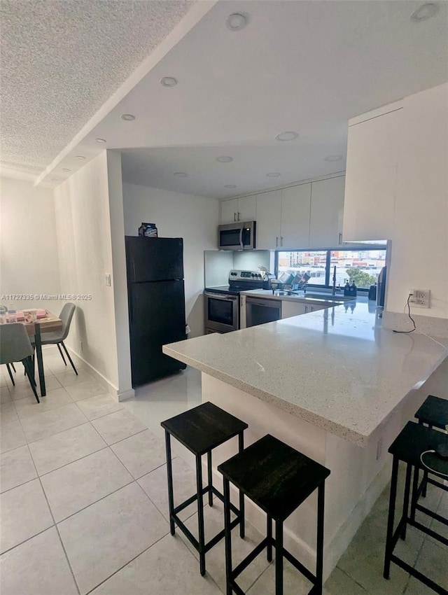 kitchen with white cabinets, appliances with stainless steel finishes, a kitchen breakfast bar, kitchen peninsula, and light tile patterned floors